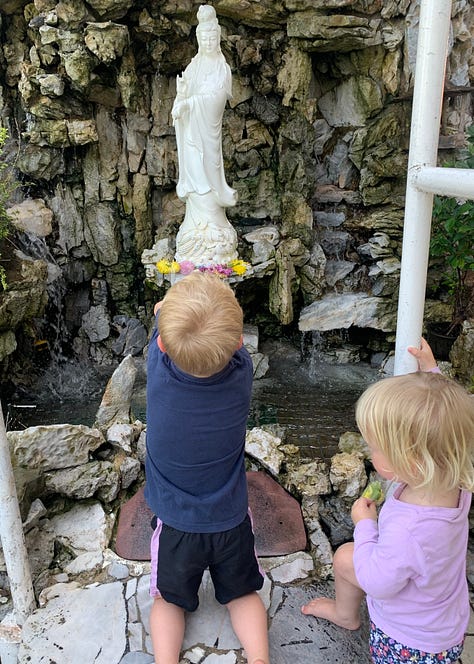 Two children aged 2 and 4 throw flowers into a fountain at a Chinese temple; red lanterns hang overhead at Thean Hou temple; a statue of an oxen in the garden at the temple.