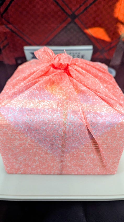 Colorful Japanese dishes inside of an obento lunch box. The box wrapped in a pink furoshiki cloth. An illustrated map inside the cover.