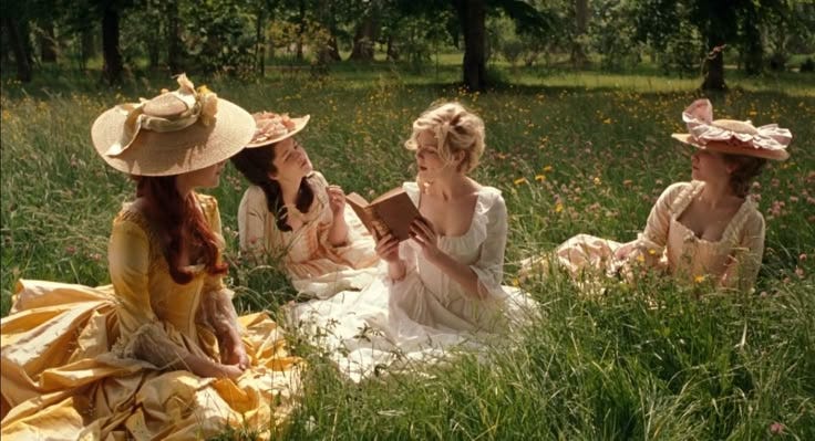 This may contain: three women sitting in the grass talking to each other while one woman is holding a book