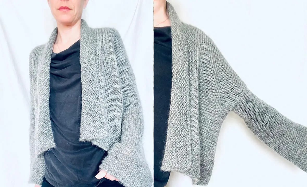 A woman stands, wearing a gray knitted oversized cardigan over a black top and jeans.