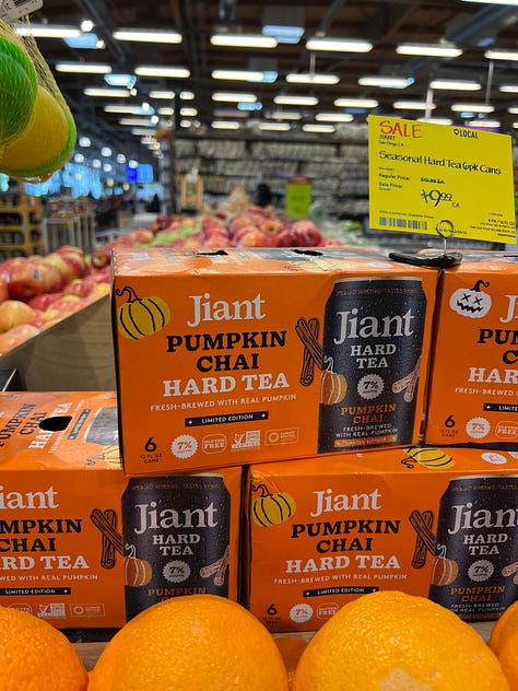 A grid of six photos of pumpkin-flavored products on shelves at an American Whole Foods: pumpkin spice grain-free cereal, pumpkin spice popcorn, pumpkin spice oat milk, cans of pumpkin chai hard tea, pumpkin spice oat bites and a pumpkin almond flour pancake mix.