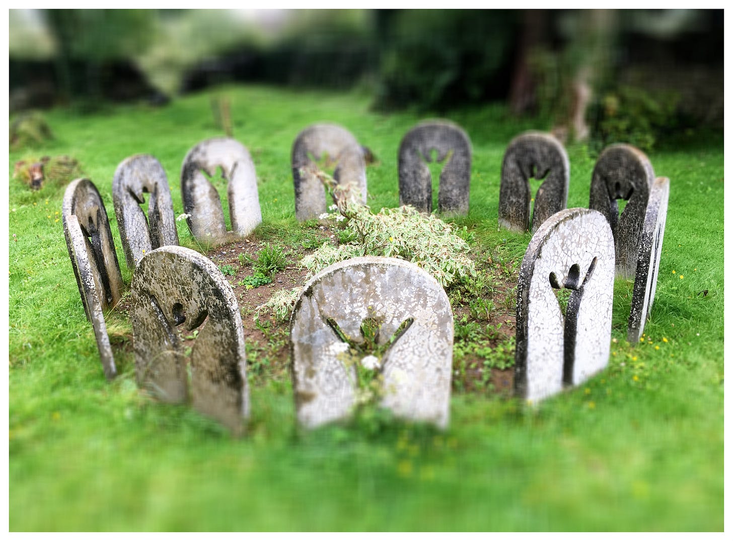 A circle of flat headstone-like objects around a raised mound of earth set in the green grass A circle of flat headstone-like objects around a raised mound of earth set in the green grass