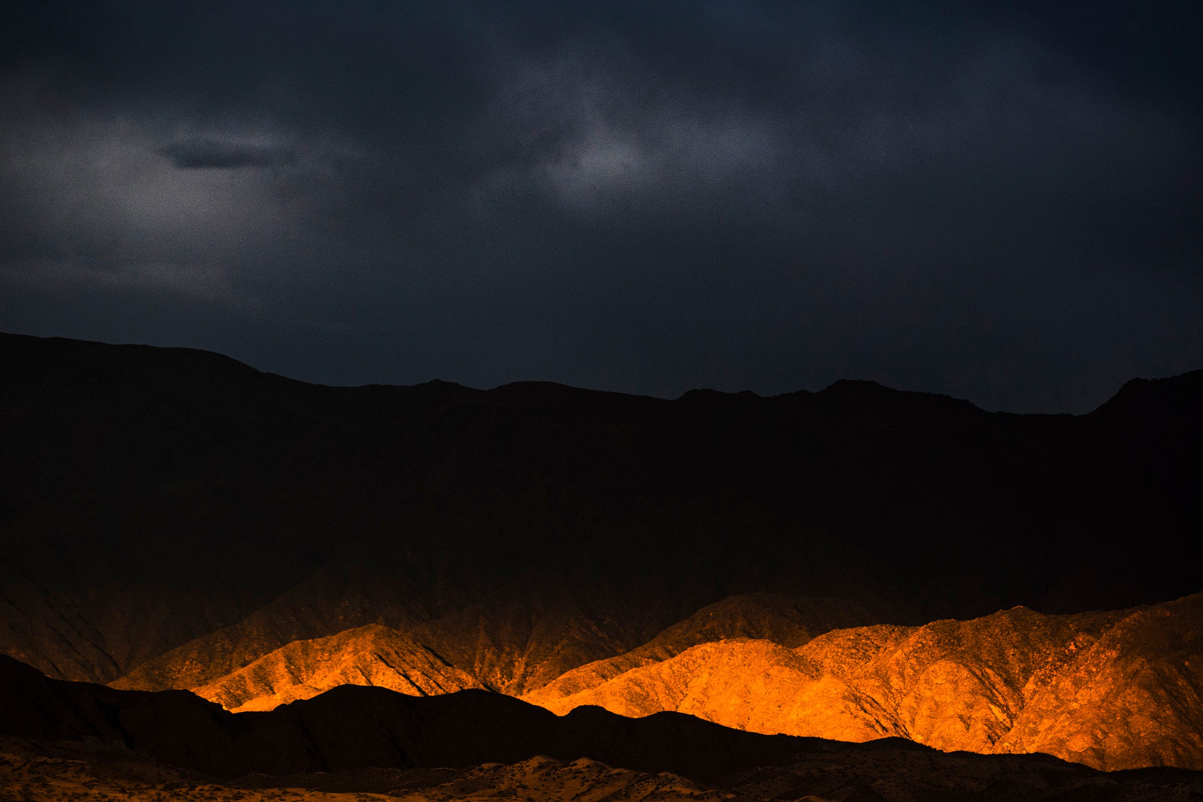 Dramatic dark clouds loom over rugged mountains, with a warm golden light illuminating the lower hills, creating a striking contrast between light and shadow in the landscape. Dramatic dark clouds loom over rugged mountains, with a warm golden light illuminating the lower hills, creating a striking contrast between light and shadow in the landscape.