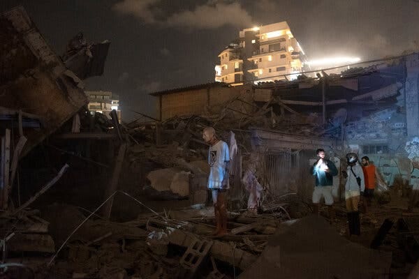 A handful of people stand in what appears to be a crater or pit at night, with a lit building above and behind them.