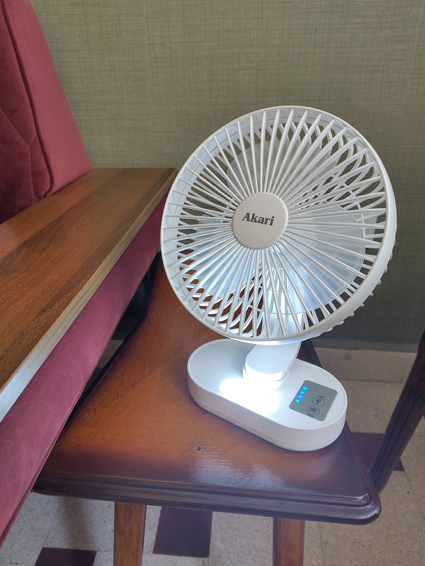 A small white fan sits on a side table next to a burgundy sofa.