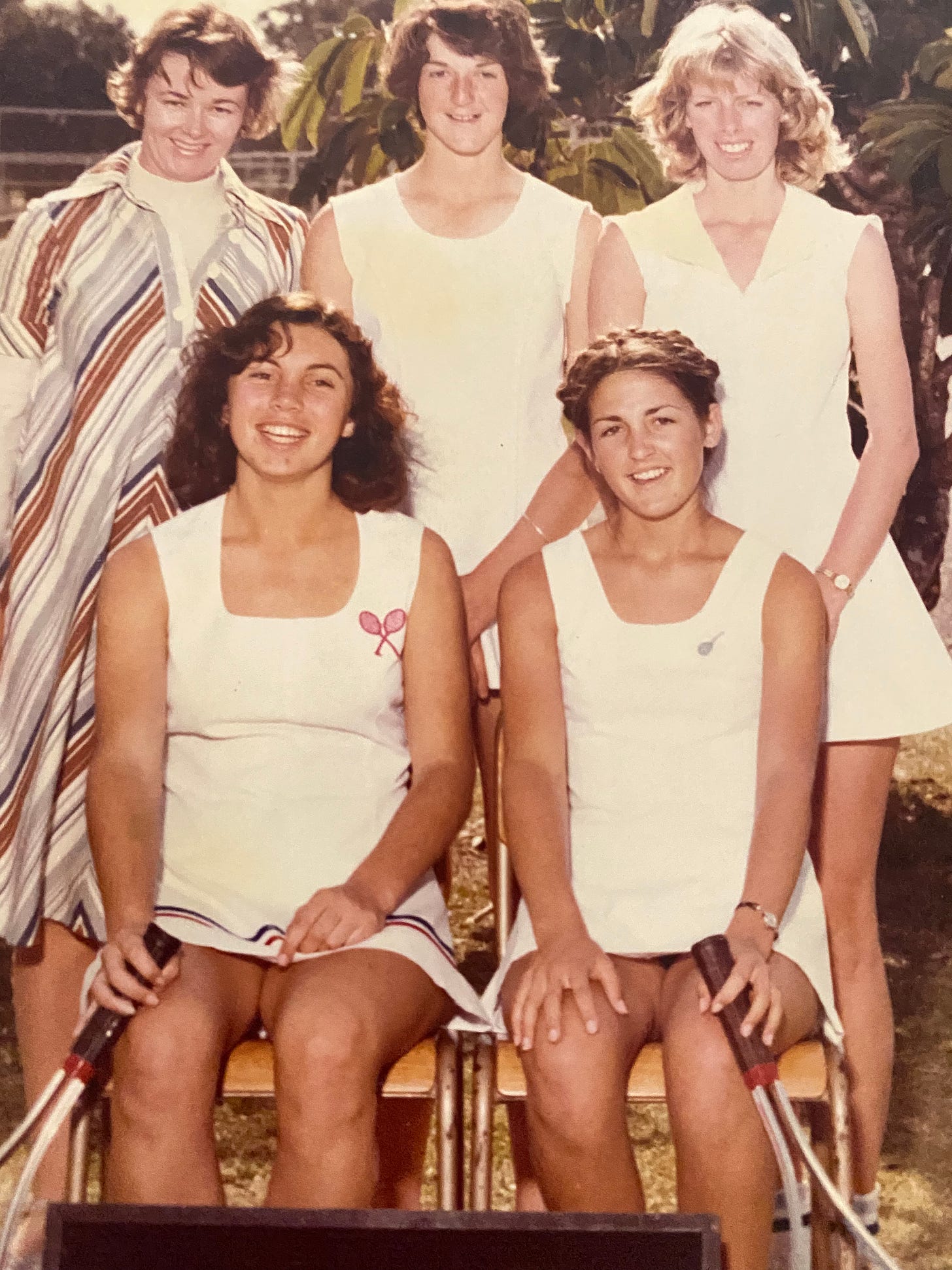 Four young women tennis players and their teacher-coach pose for school photo.