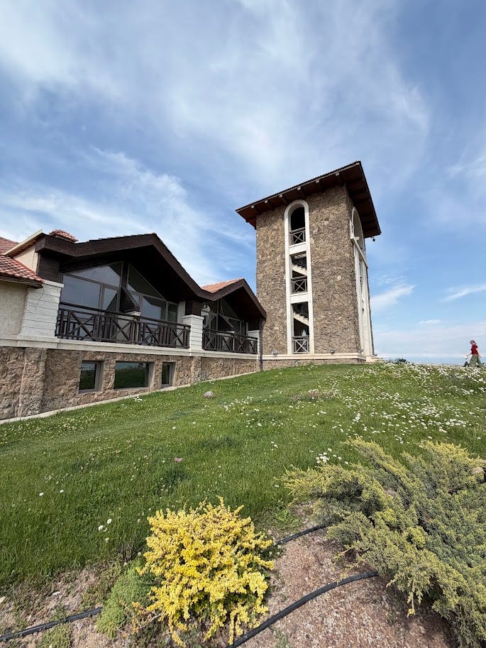 Van Ardi's stone estate building and belltower overlooking green hillside gardens, alongside a collection of empty Van Ardi and Tor-Tori wine bottles gathered under a tree after tasting