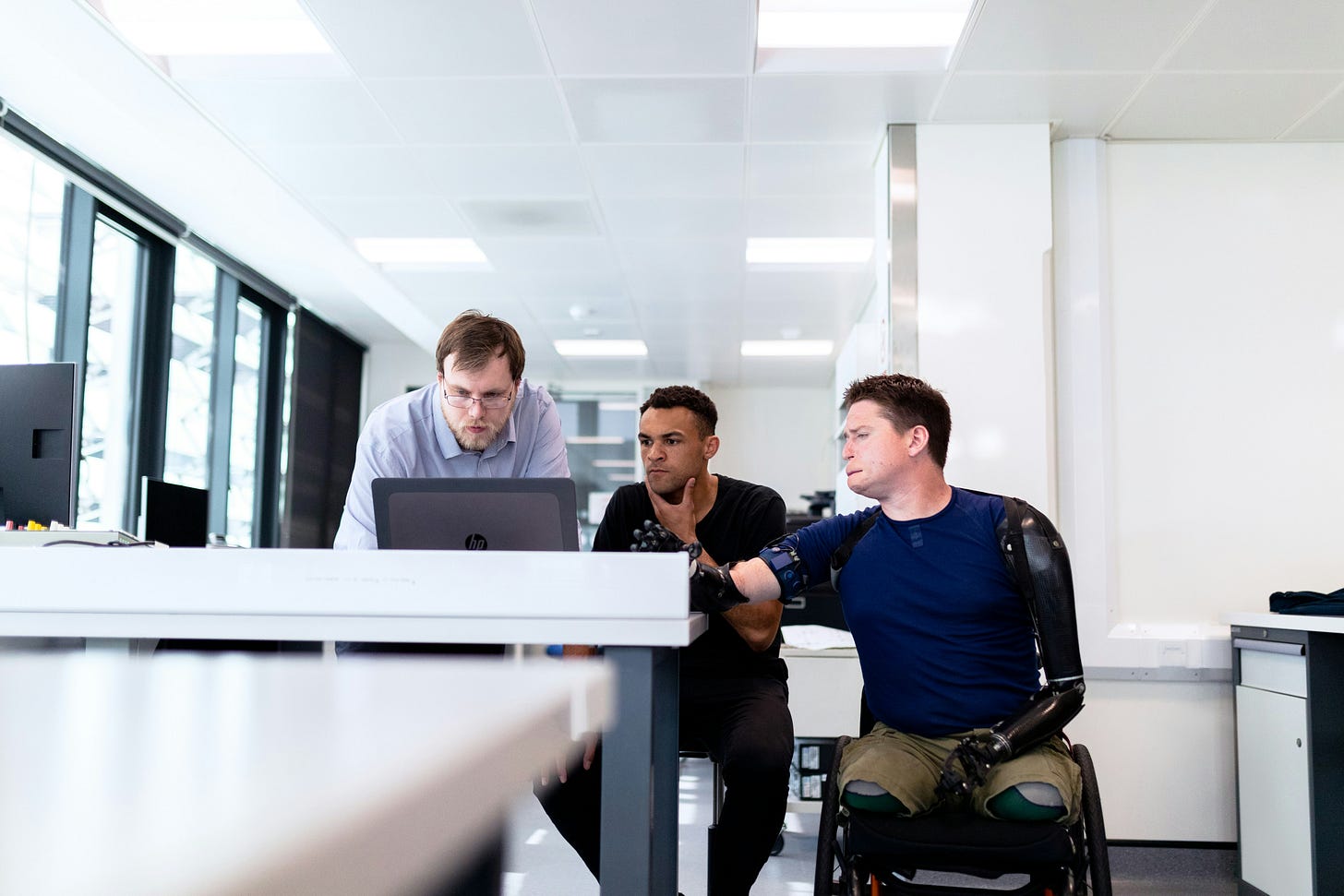 Three engineers look at computer screen with prosthetic limb user.