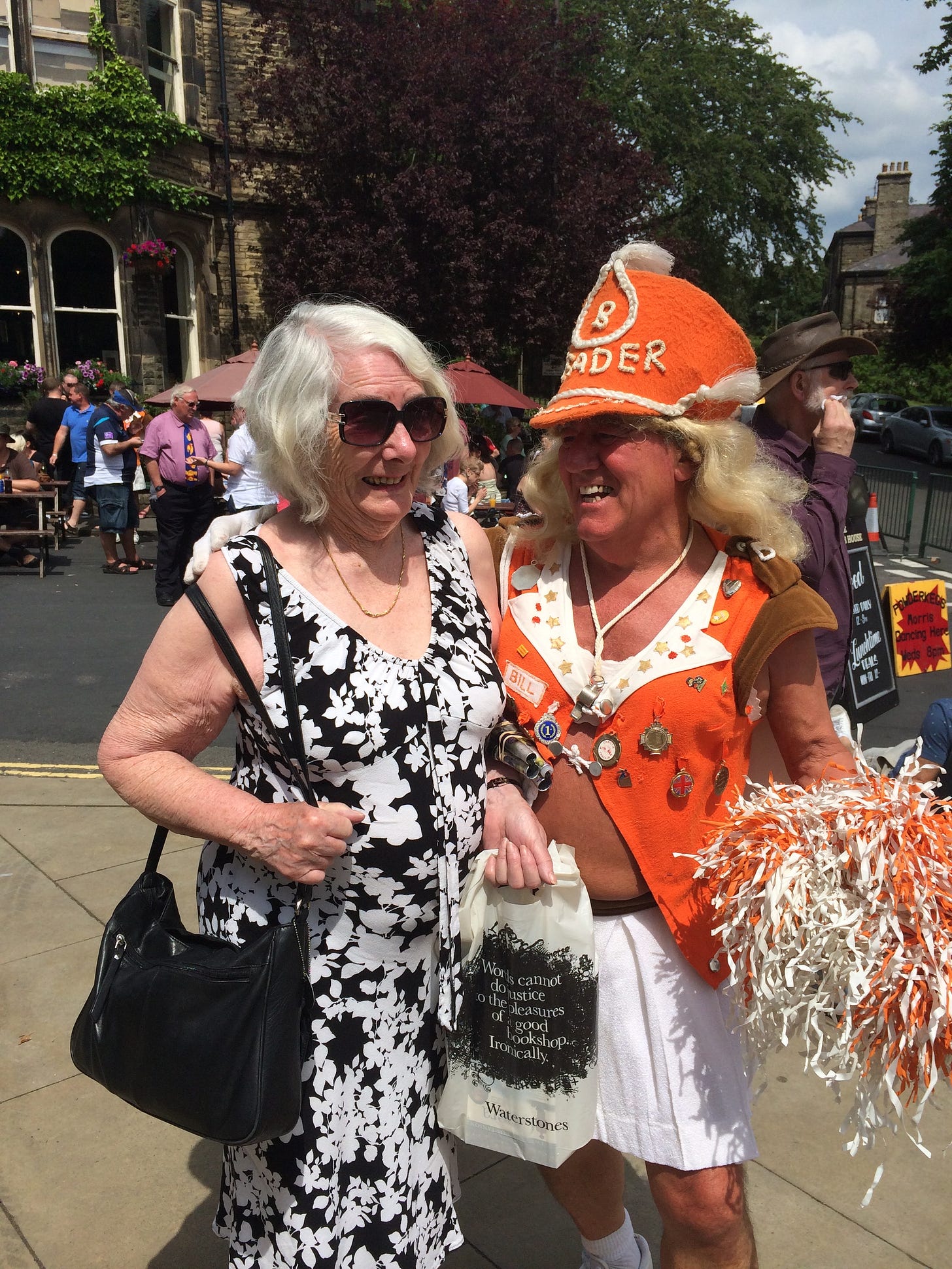 A woman is laughing, she is with a man dressed as a majorette, he is also laughing.