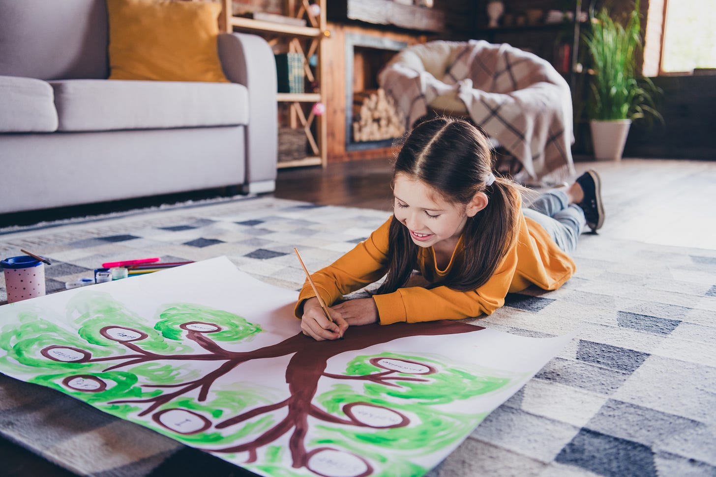 Girl lying on the living room floor painting a family tree.