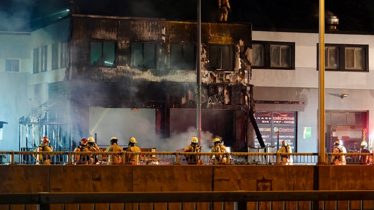 Firefighters spray water at a burnt commercial building.
