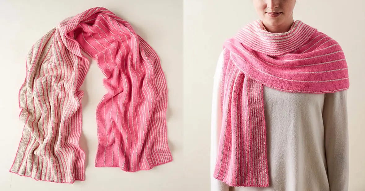 A woman stands, wearing a pink and white striped double-knitted scarf and a white sweater.