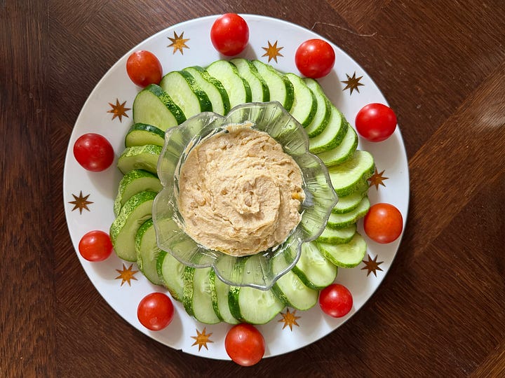 A man on a yellow ride-on mower on a green lawn; a barefoot boy walking a slackline between trees; a bowl of freshly picked cherry tomatoes with a zucchini; a plate of cucumber slices around hummus.