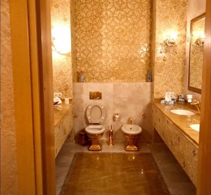 A bathroom with gold fixtures, including a toilet, bidet, toilet brush, and sink fittings, featuring gold mosaic tile walls. A bathroom with gold fixtures, including a toilet, bidet, toilet brush, and sink fittings, featuring gold mosaic tile walls.