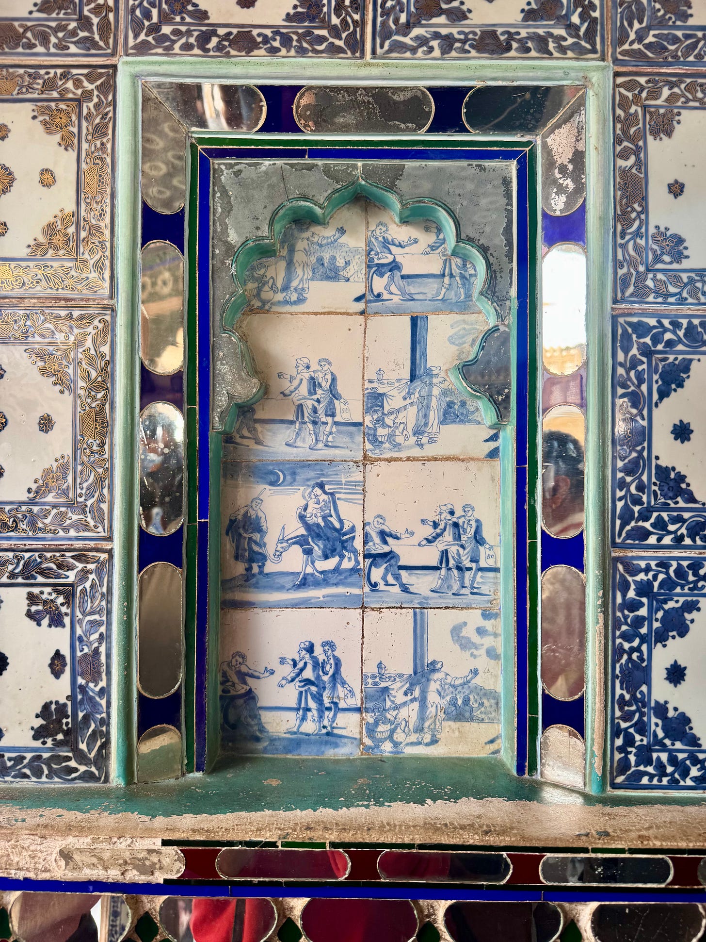 Close-up of a niche lined with blue-and-white tiles depicting small figures in scenes.