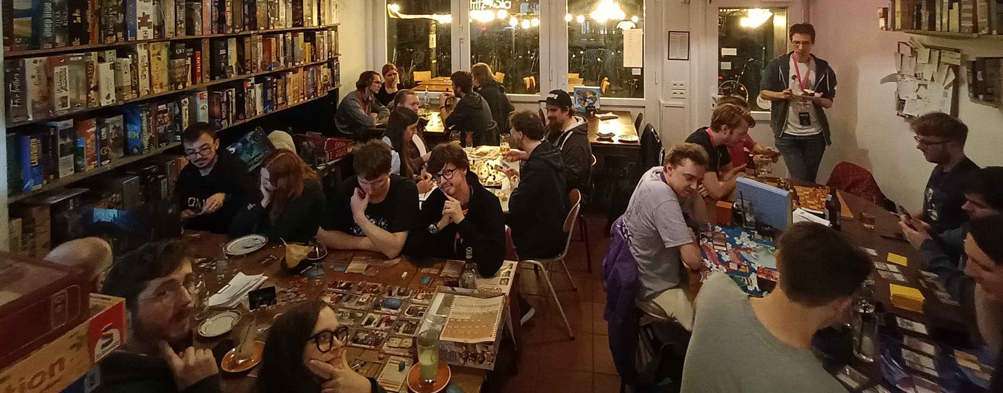Many attendees are split across four large tables while playing board games in a board game café in Cologne Many attendees are split across four large tables while playing board games in a board game café in Cologne