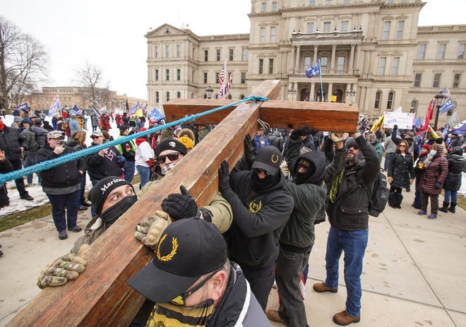 Members of the Proud Boys and others help James Chapman of Belleville raise a large red cedar cross he brought as hundreds of Trump supporters gather outside of Michigan’s State Capitol building in Lansing on Wednesday, January 6, 2021 during a rally to pray for Trump.