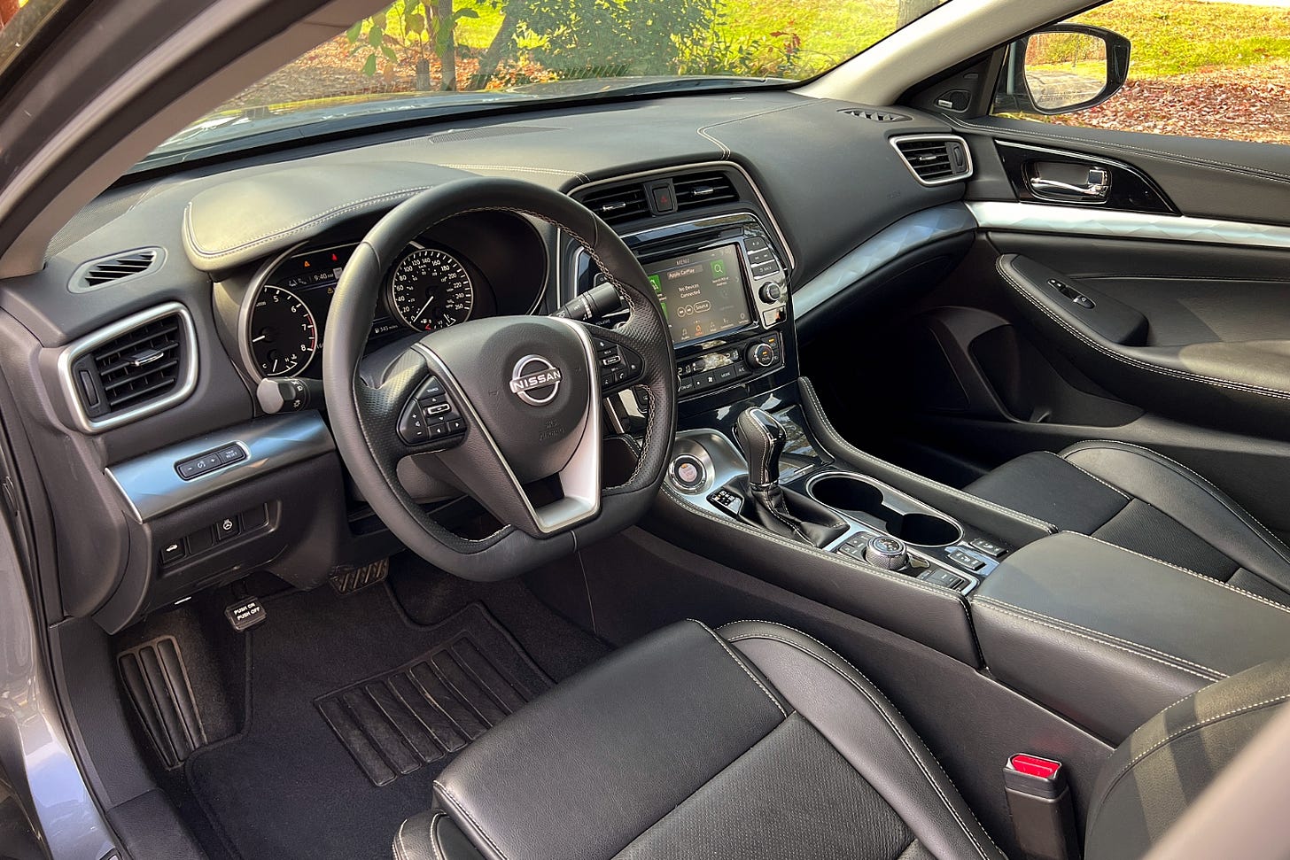 View of a Nissan Maxima interior showing the dashboard and black leather front seats.