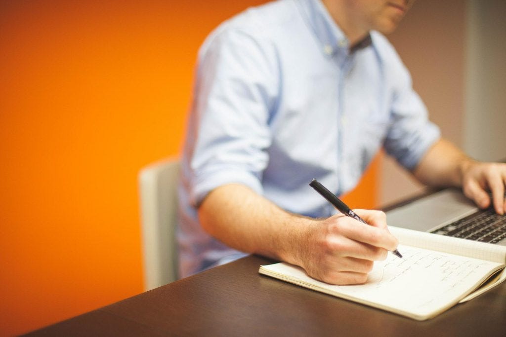 man in white business shirt writing on paper at a desk. man in white business shirt writing on paper at a desk.