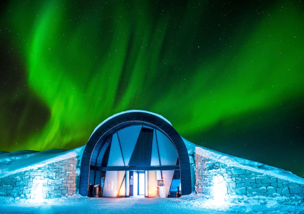 ICEHOTEL illuminated at night beneath the Northern Lights in Swedish Lapland.