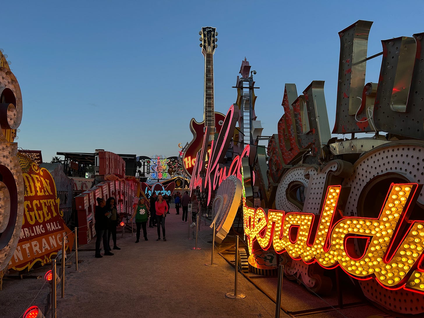 An outside corridor with people walking; there are various signs and neon signs on both sides of them