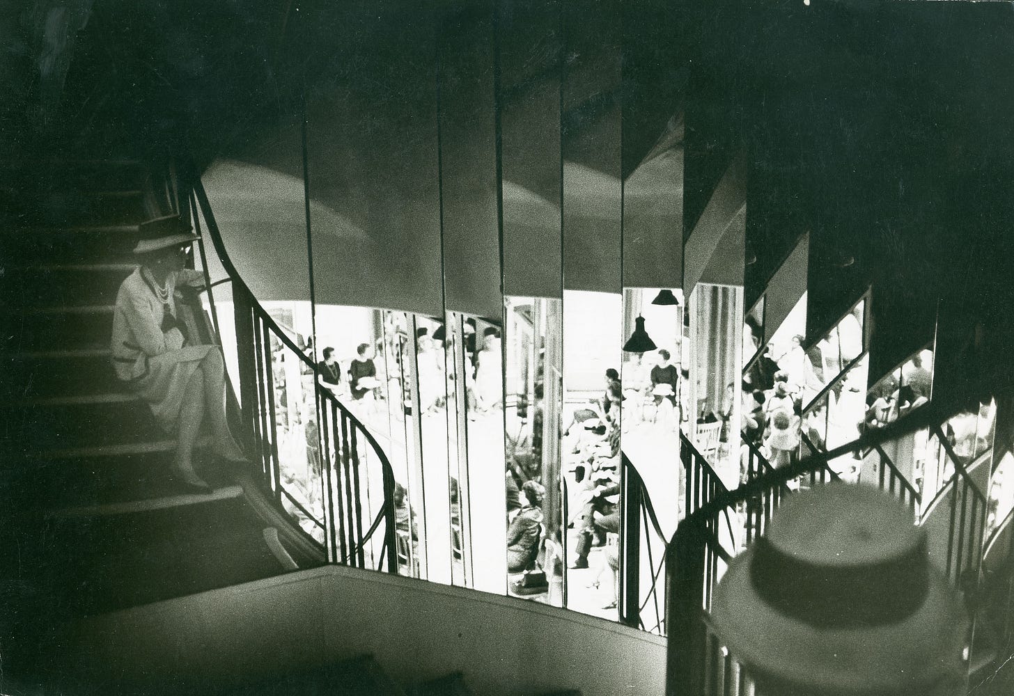 Designer Coco Chanel sits overlooking the mirrored spiral staircase of her store.