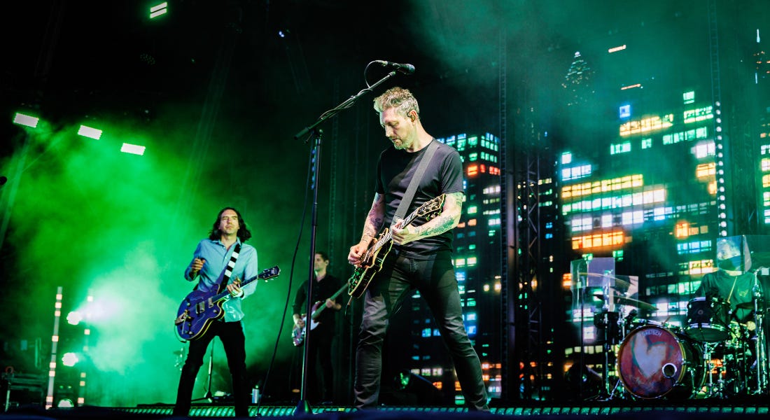 A stage with green lights and band members playing guitar A stage with green lights and band members playing guitar