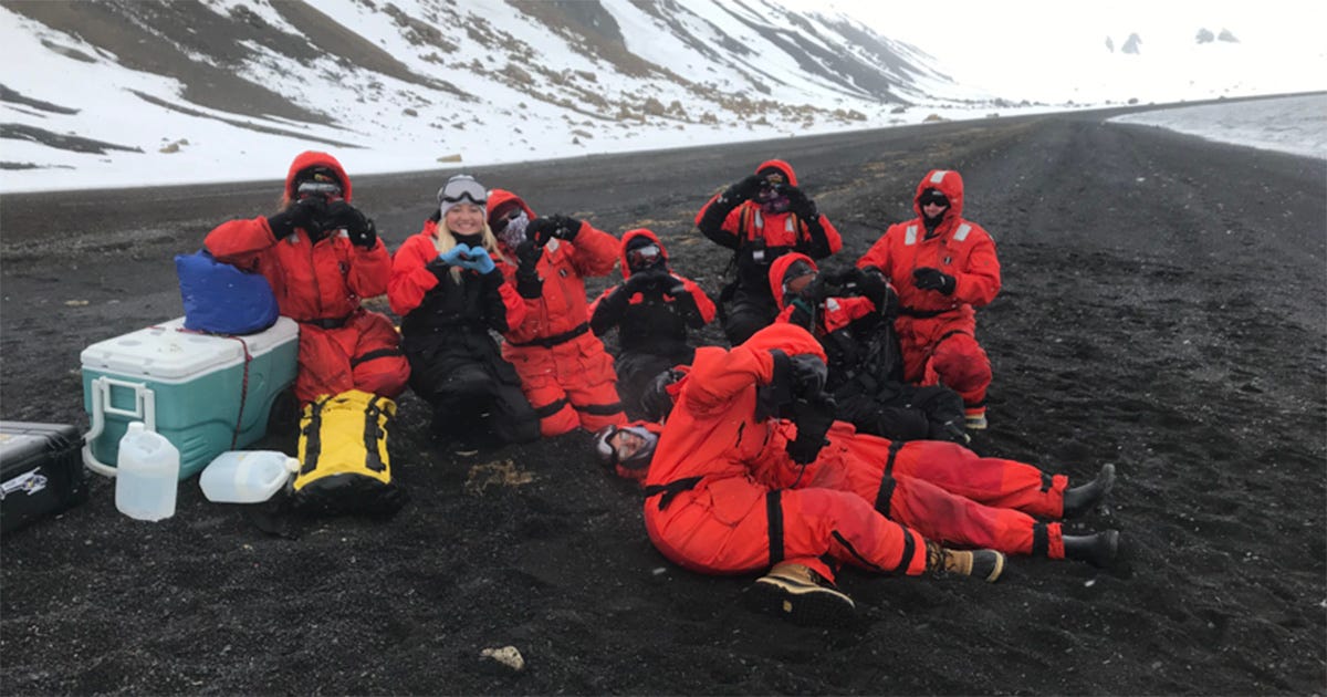 Grupo de pesquisadores na Antártica com trajes de inverno laranja.