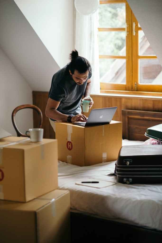 ethnic man typing on laptop while preparing to relocate