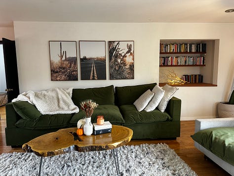 each photo is of Andrea and Meg's living room, painted in progressively different colors with slight alterations on decor at well. In first photo, wall is charcoal colored. Subsequently, emerald, light pink, wallpapered, white with a "stay tender sign", then white with a triptych of cacti.