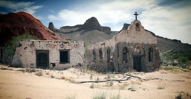 A decaying desert chapel with a broken cross, surrounded by dry scrubland and distant mountains. The church walls are crumbling, symbolizing the collapse of once-sacred structures. The image evokes abandonment, failure of leadership, and the spiritual consequences of masculine retreat.