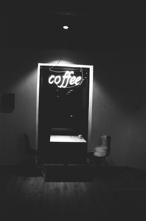 1) A black & white photograph of a photograph, which contains a large sign on the side of the road reading: "HELLO STRANGER" in capital letters. 2) A scattered pile of multi-coloured books overlayed with sheer, green pattered cloth. 3) A black & white photograph of café chairs & tables crammed against a wall. 4) Scattered, multi-coloured books. 5) A black & white photograph of a wooden deck in an alleyway. Lights are strung across both the deck & alleyway. 6) An ink drawing of a map of a fantasy land. 7) A black & white photograph of two chairs & a table next to a window. A neon sign reading "coffee" is above them. 8) A black, mauve, and dark green watercolour painting of a bare forest. Beneath the painting are the words "magic forest" in calligraphy. 9) A black & white photograph of the roof of an ornate building, mirroring itself at the top & bottom of the image.