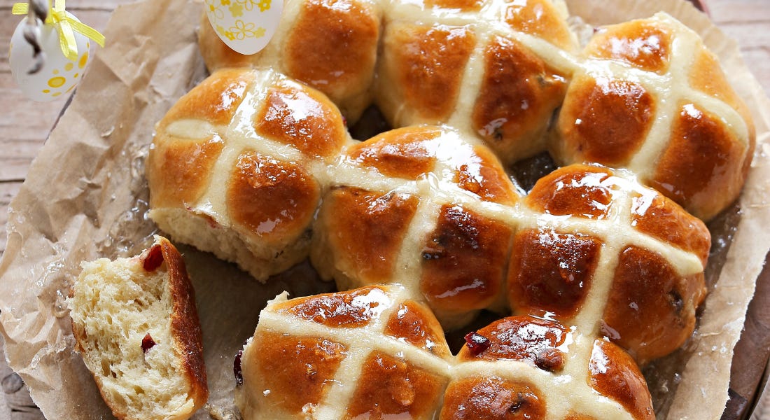 A tray of hot cross buns with paper on the bottom and the one to the bottom left torn A tray of hot cross buns with paper on the bottom and the one to the bottom left torn