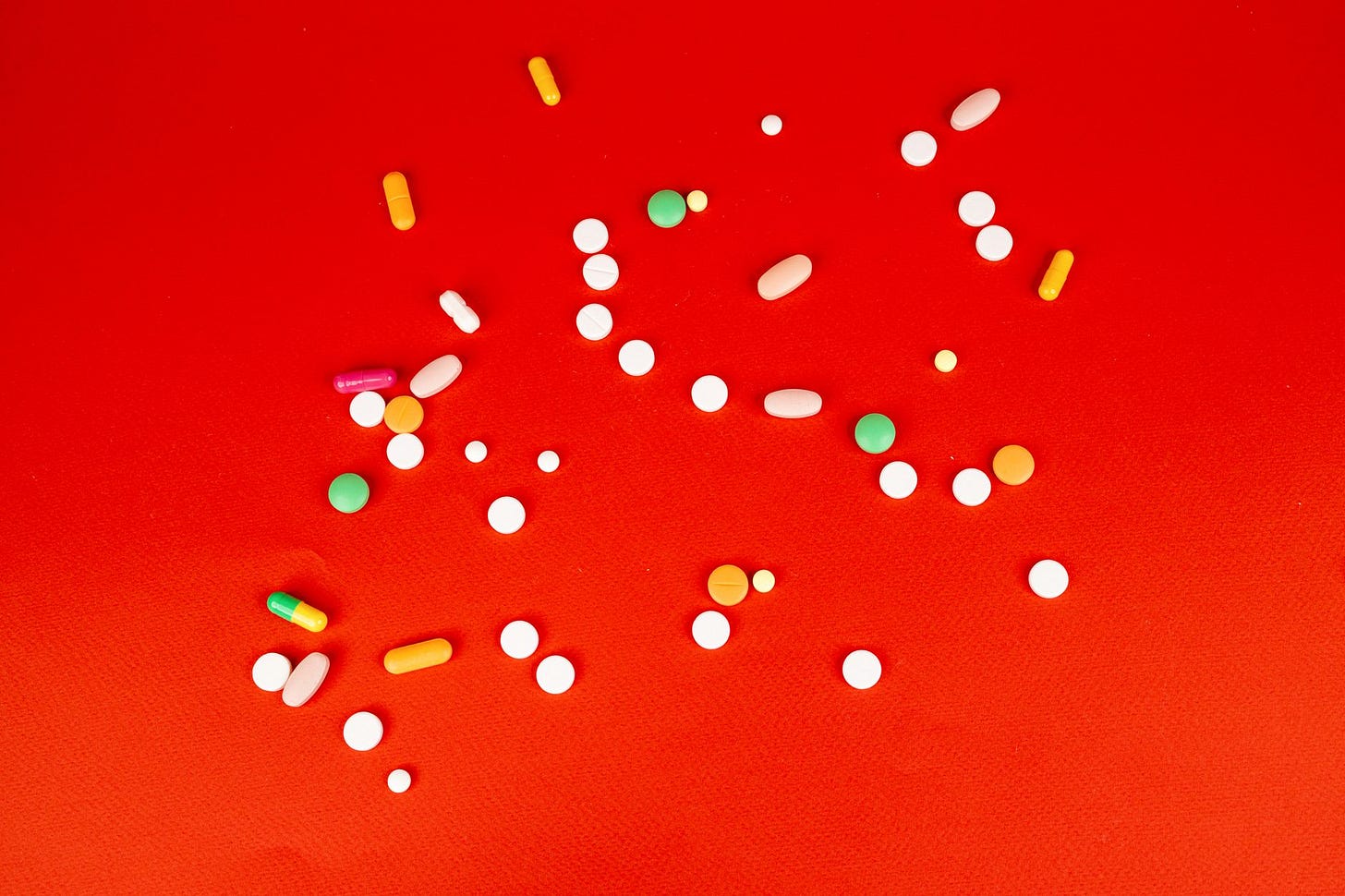 Photo by Maksim Goncharenok on Pexels A colorful assortment of pills and capsules scattered on a bright red surface. Healthcare and medication concept. (stock photo)
