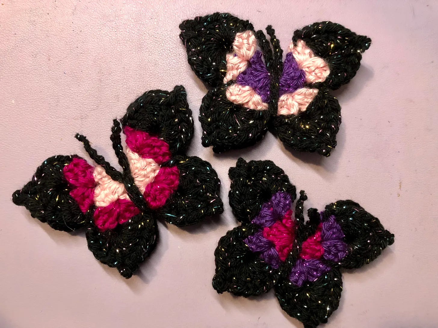 Three crochet butterflies with black, pink, and purple yarn.