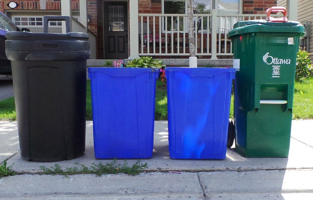 Photo of a black bin, two blue bins, and a green bin Photo of a black bin, two blue bins, and a green bin