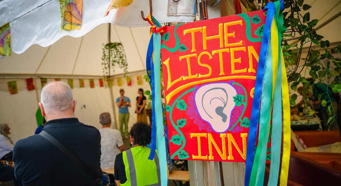 A red sign that says 'the listen in' hanging on a white canopy with people standing inside A red sign that says 'the listen in' hanging on a white canopy with people standing inside
