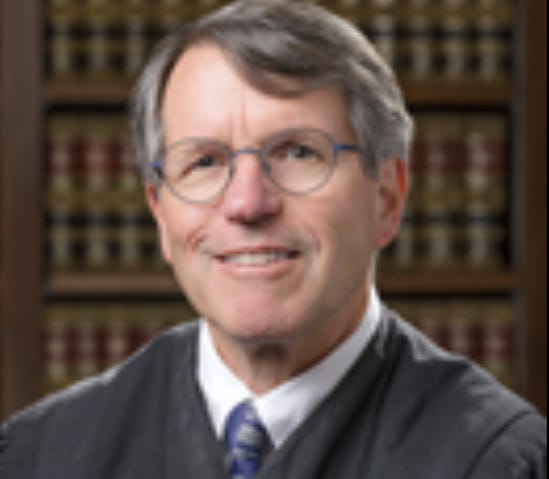 A person wearing glasses and a black robe

AI-generated content may be incorrect.