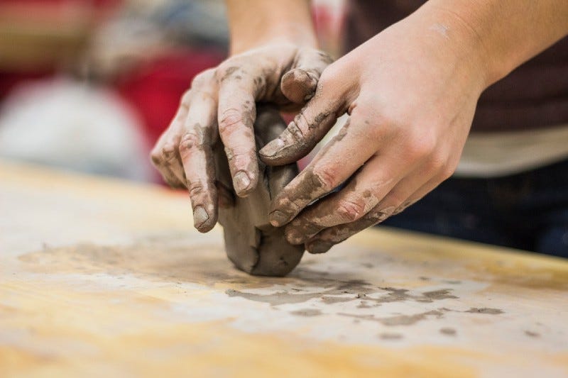 Image of two hands molding clay to form an object Image of two hands molding clay to form an object