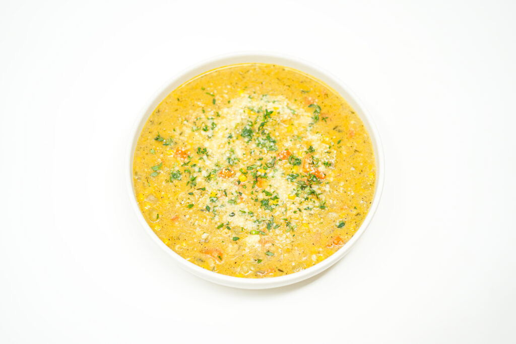 A bowl of creamy corn clam chowder garnished with fresh thyme and grated Parmesan, showcasing the rich, velvety texture and vibrant pops of sweet corn and tender clams.