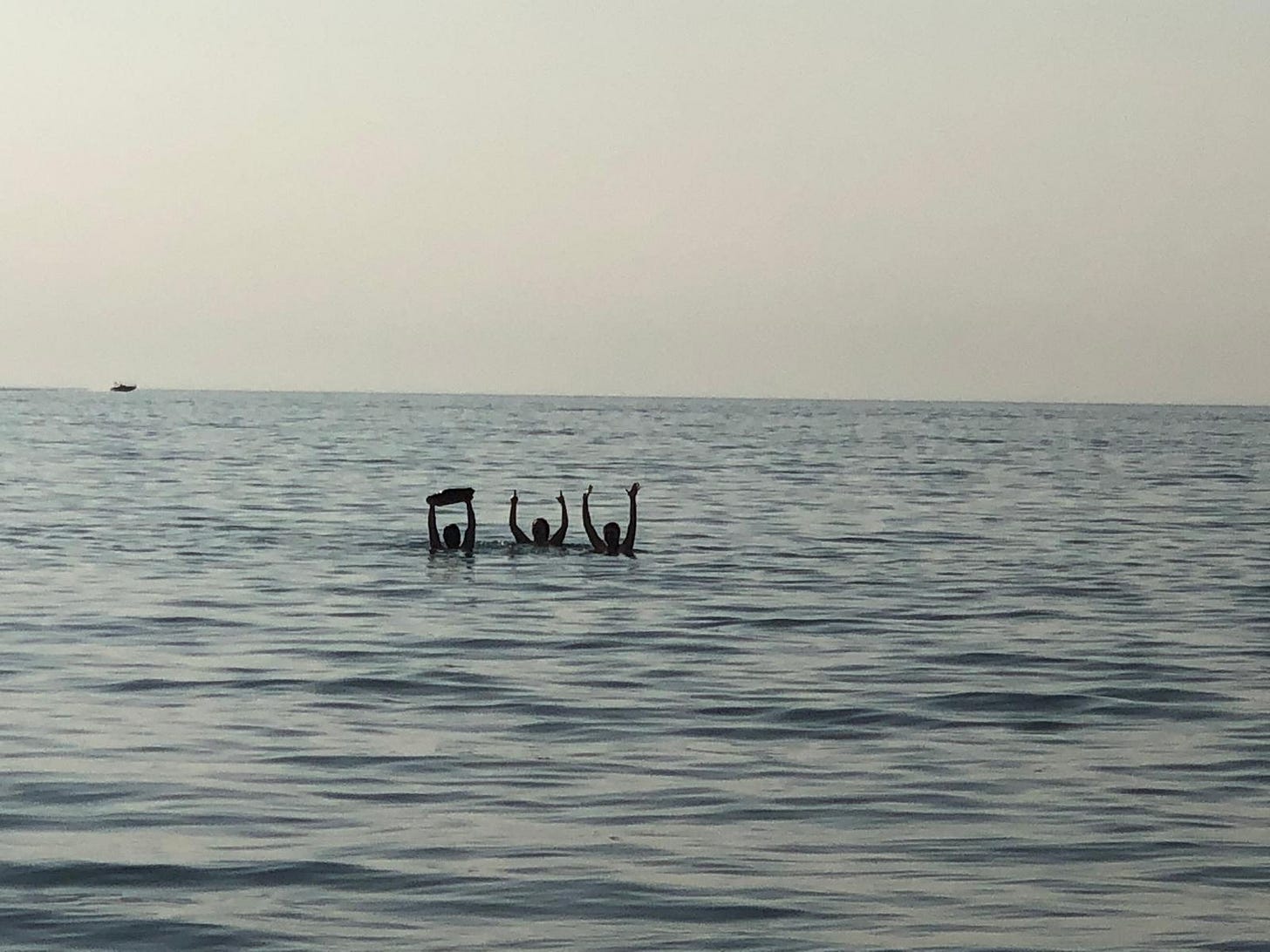 N, C, and Jo in the water of Lake Erie, N holding a rock over his head while C and Jo wave to me