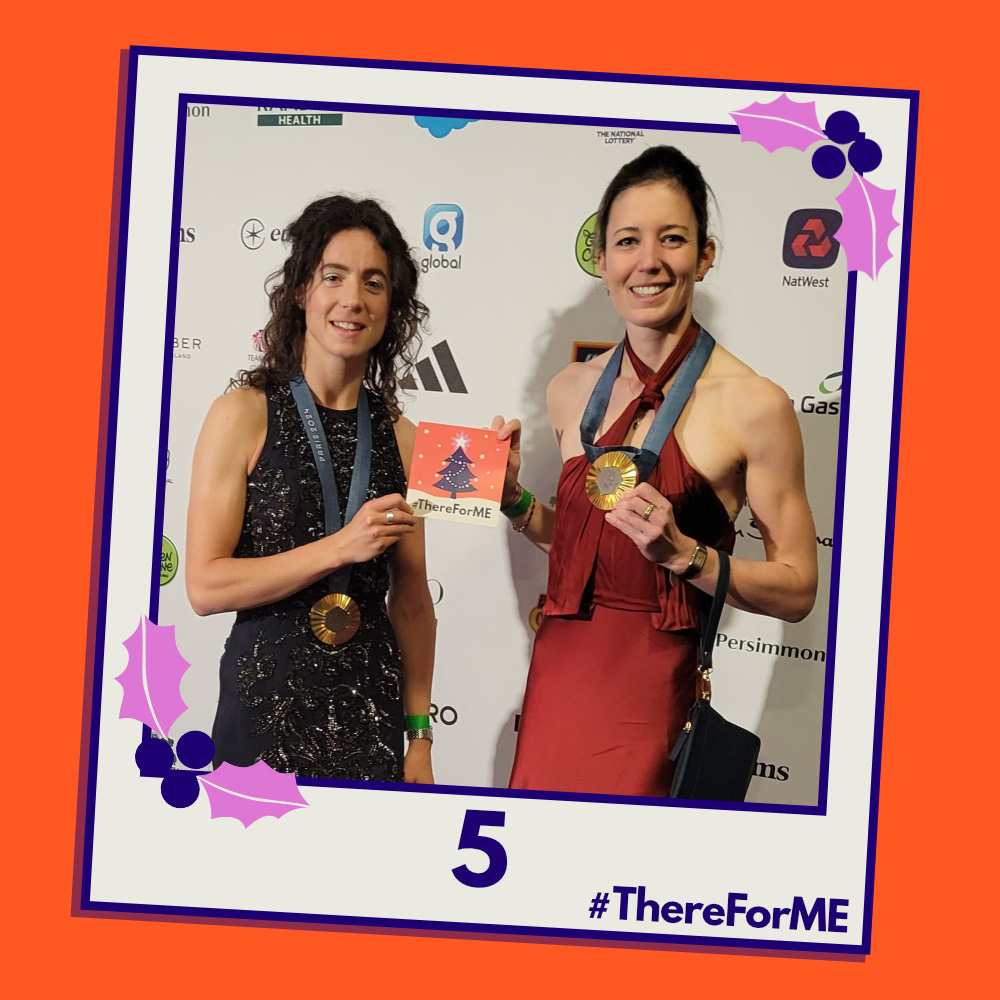 A pretend polaroid shows Olympic champions Emily Craig and Imogen Grant posing for a photo wearing their gold medals and holding a #ThereForME Christmas card.   The image on the card shows the dark blue Christmas tree, decorated with sparkling fairy lights, baubles and a star on the top, in a snowy landscape against a starry backdrop. The design is in the #ThereForME colours.