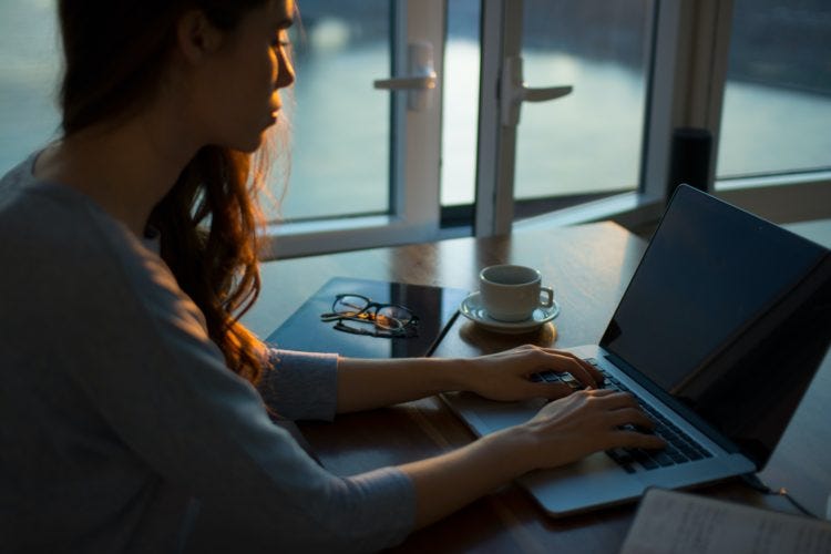 Woman types at a laptop with coffee