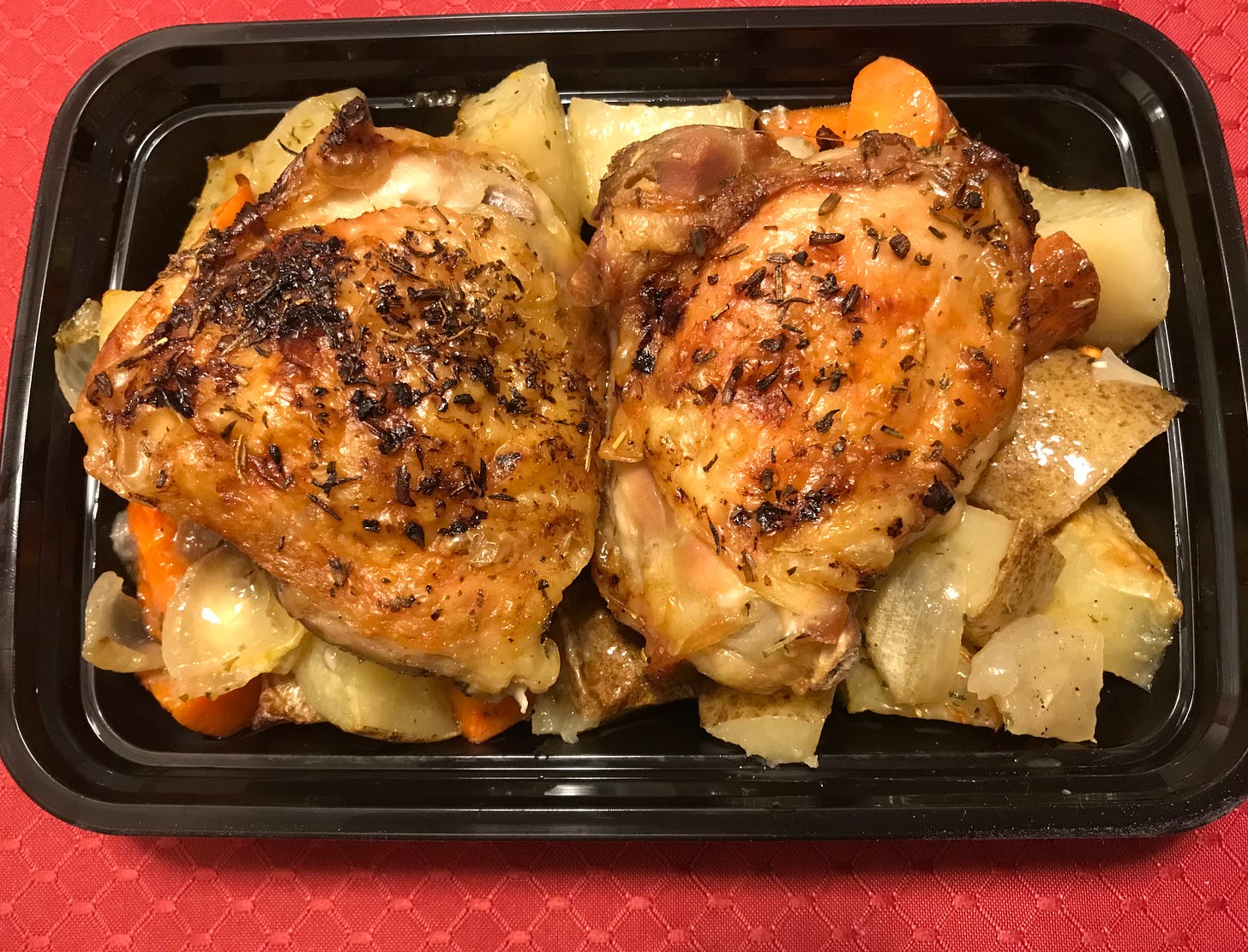 two chicken thighs atop potatoes and carrots in to-go container
