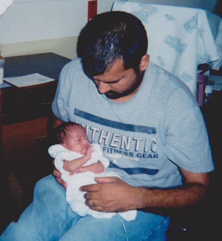 A man cradling a newborn baby in a hospital chair