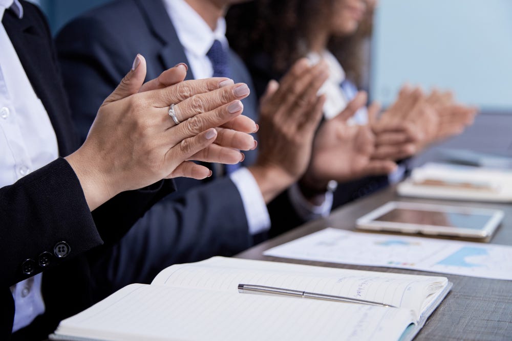 Several people sitting at a table in a row, clapping, their faces are not visible, there are notebooks open in front of them. Several people sitting at a table in a row, clapping, their faces are not visible, there are notebooks open in front of them.