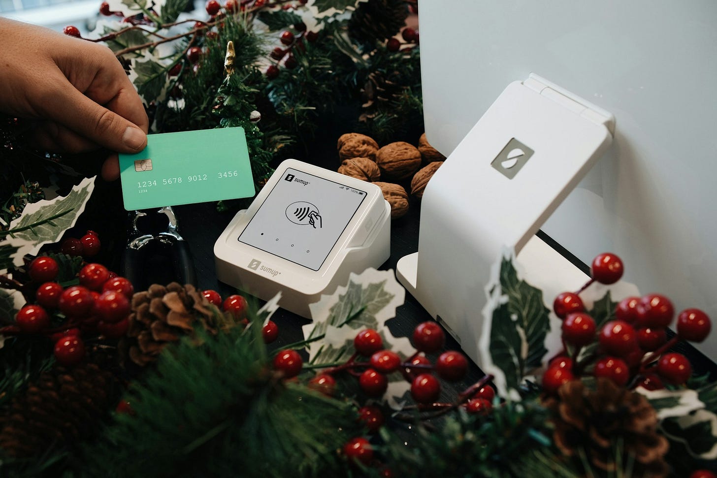 A customer holds a payment card near a contactless reader surrounded by holiday decorations, symbolizing small-business holiday sales. Photo by SumUp on Unsplash