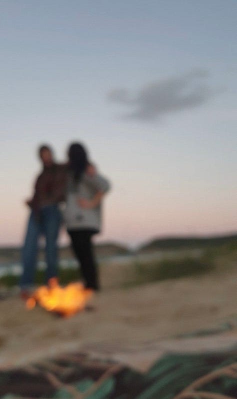 two women having fun behind a fire on the beach
