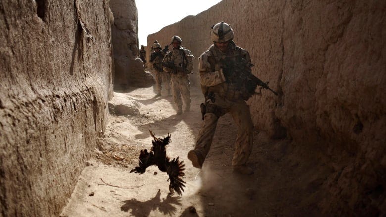 Armed soldiers walk down a narrow passageway between earth walls.