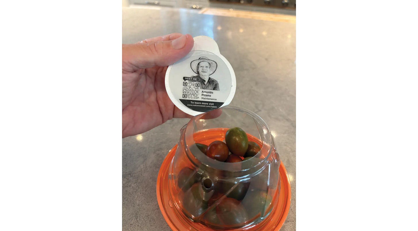 Cherry tomatoes in a plastic container, the lid has a photo of a team member and a QR code
